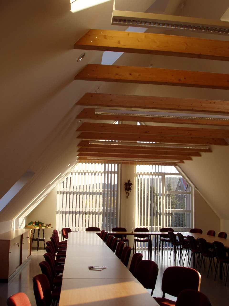Schulungsraum im Dachgeschoss mit sichtbaren Holzbalken und Fensterband im Giebel