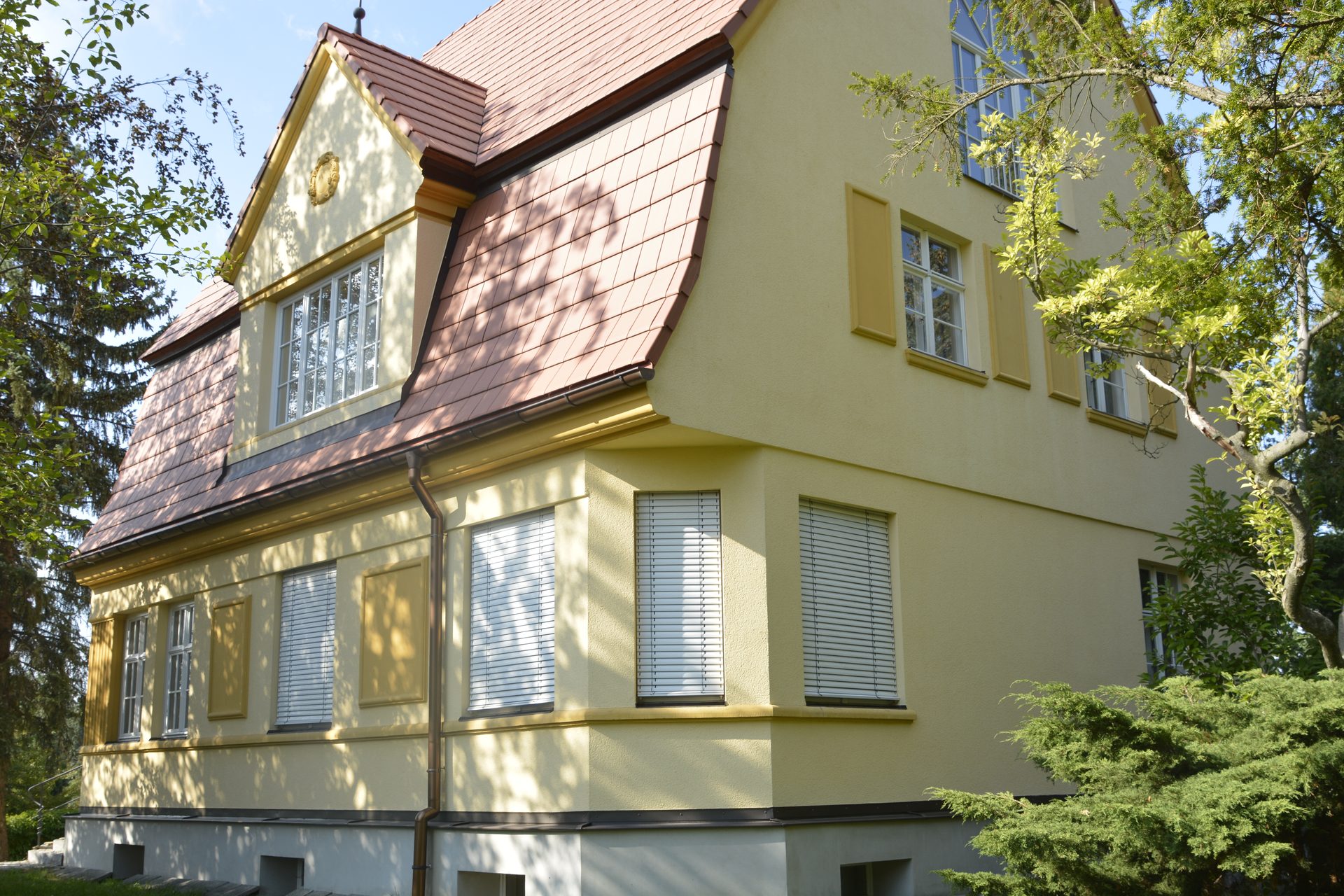 Gelbe Putzfassade der Villa mit Sprossenfenstern, Dachgaube und roter Dacheindeckung
