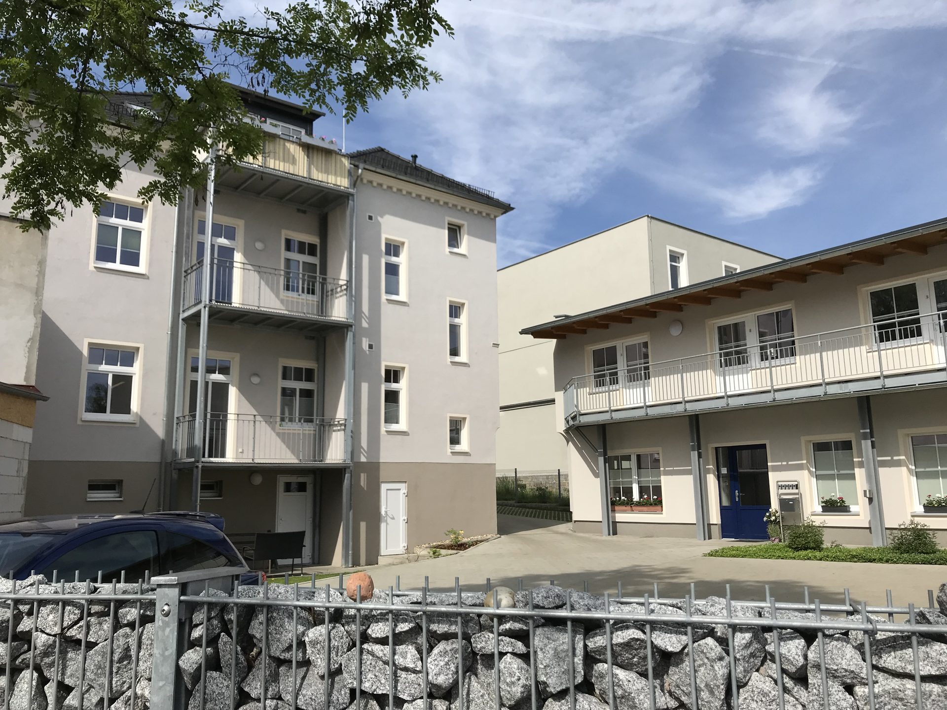 Hofsituation zwischen Stadtvilla und umgebautem Nebengebäude mit Gabionenmauer