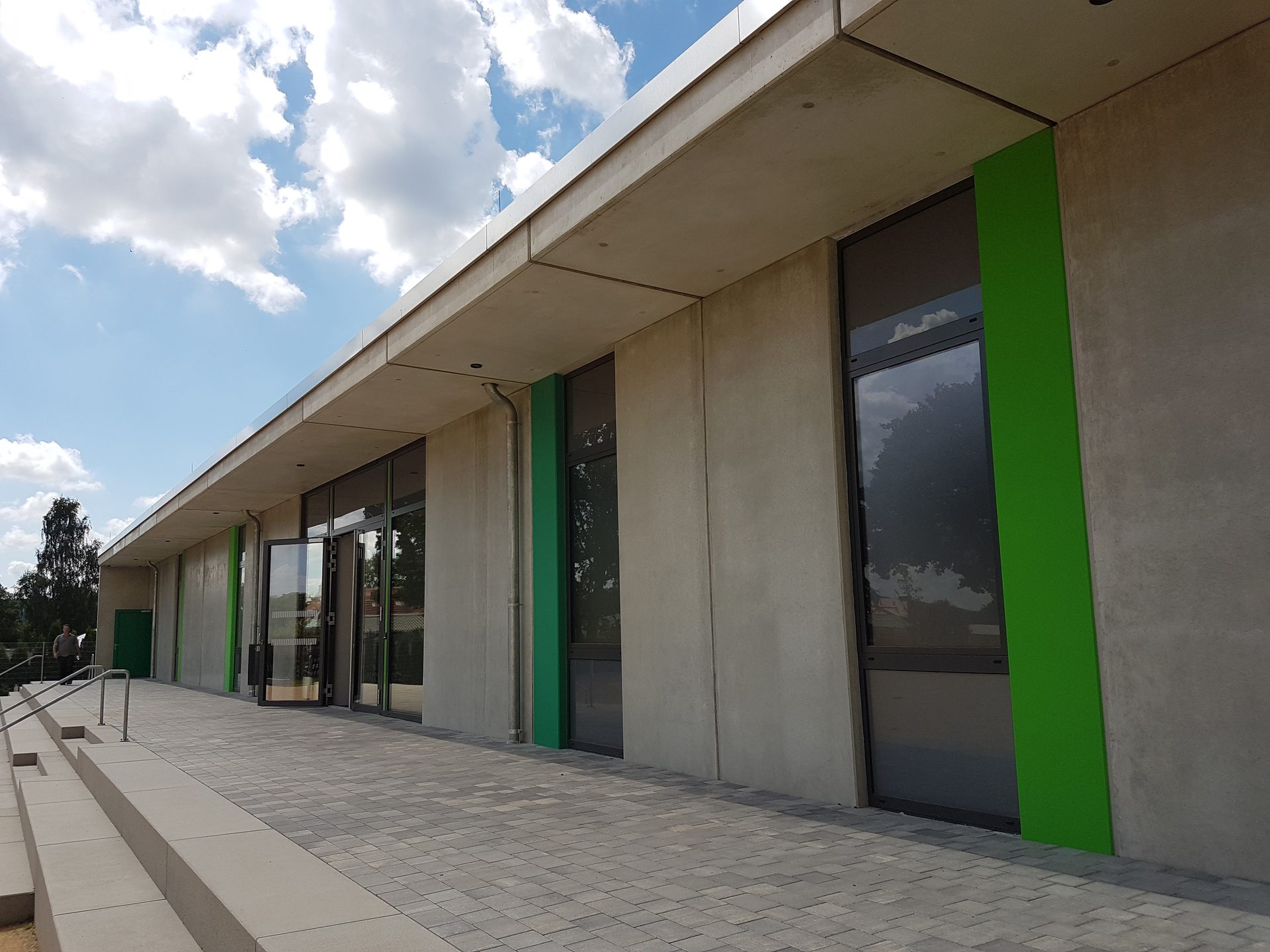 Sichtbetonfassade der Sporthalle mit grünen Glasakzenten am Eingang