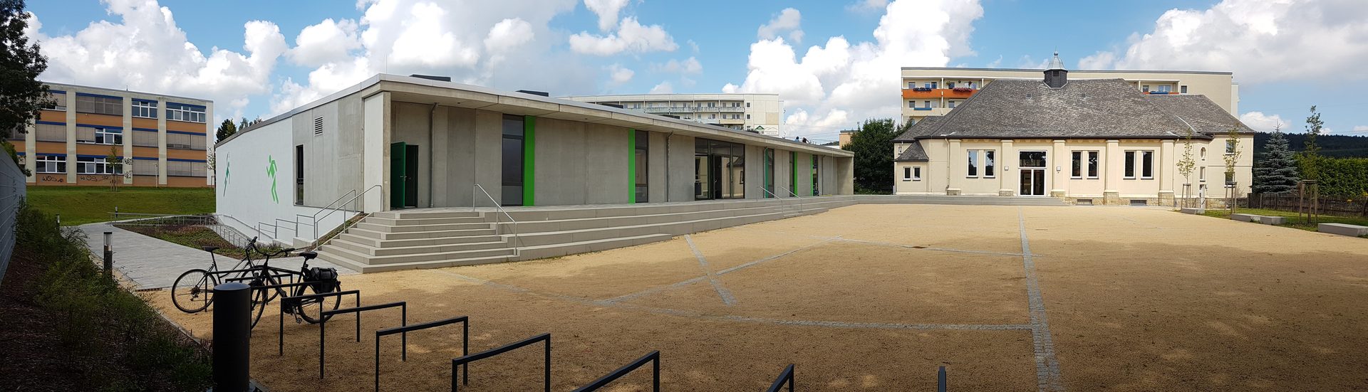 Panorama des gemeinsamen Vorplatzes vor neuer Sporthalle links und alter Turnhalle rechts
