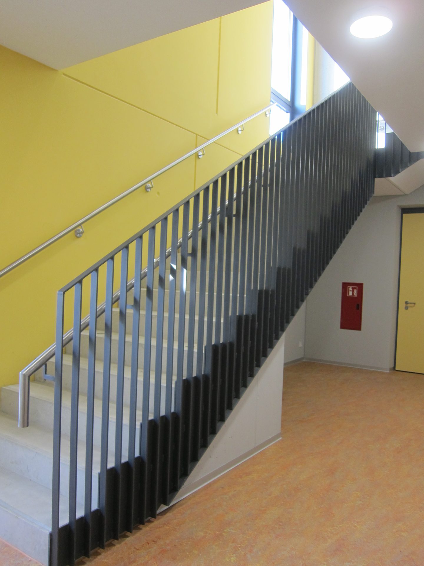 Treppenlauf im Inneren der Sporthalle mit farbig gefasster Wand