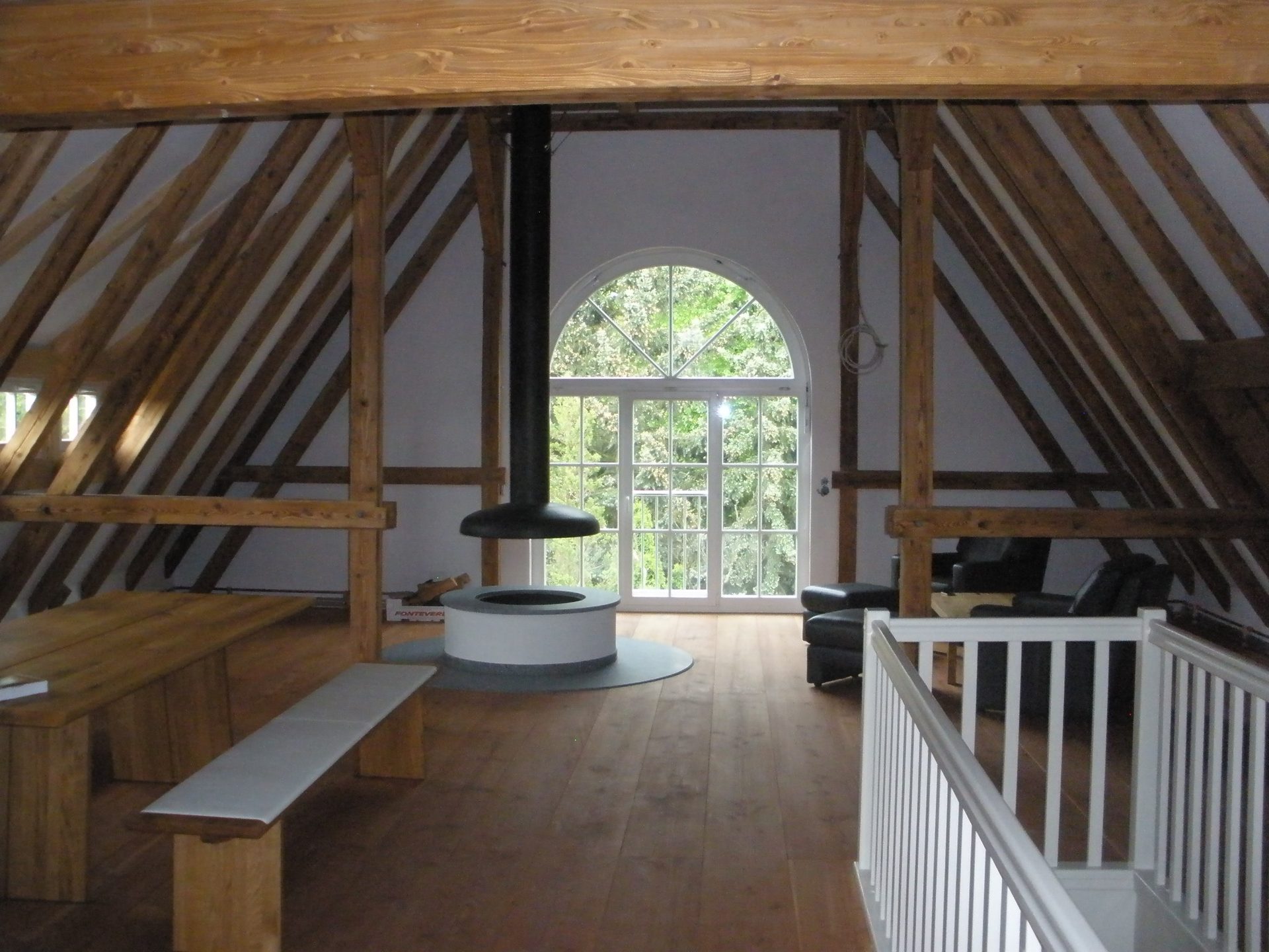 Ausgebautes Dachgeschoss mit sichtbarem Holztragwerk, Kaminofen und Rundbogenfenster
